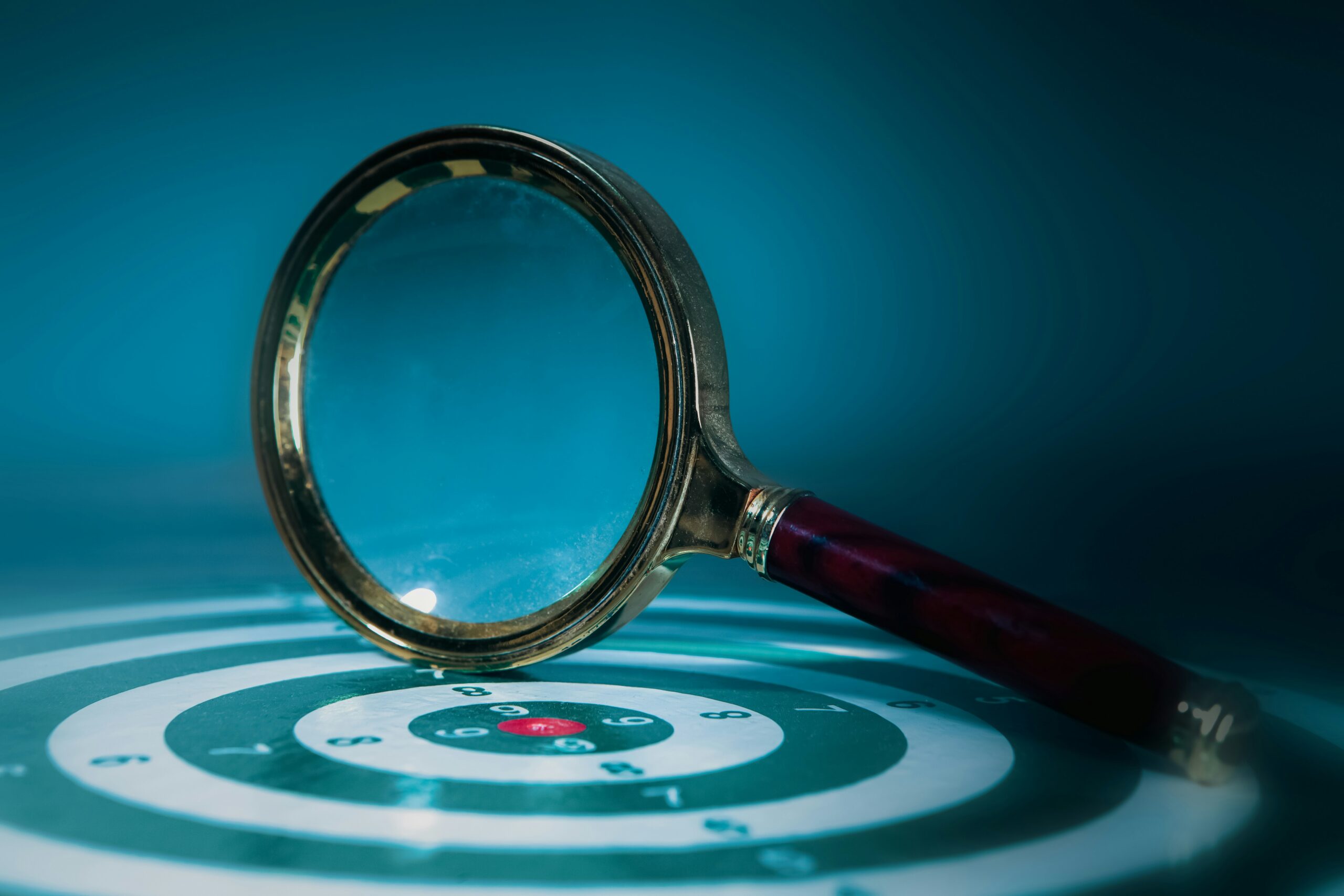 Close-up of a magnifying glass resting on a circular target with blue-green rings and a red center field.