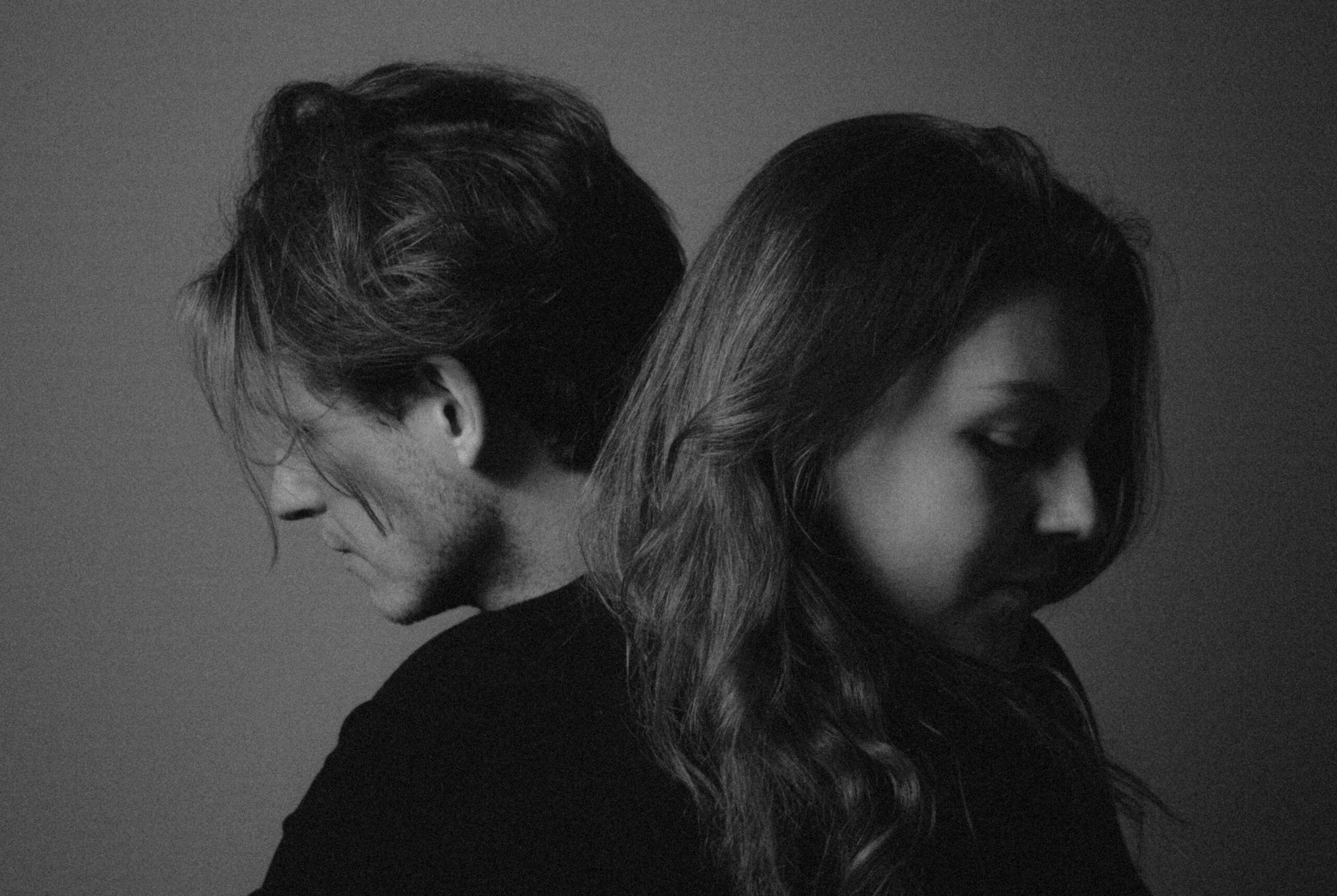 Black-and-white photo of a man and woman standing back-to-back, facing away from the camera.