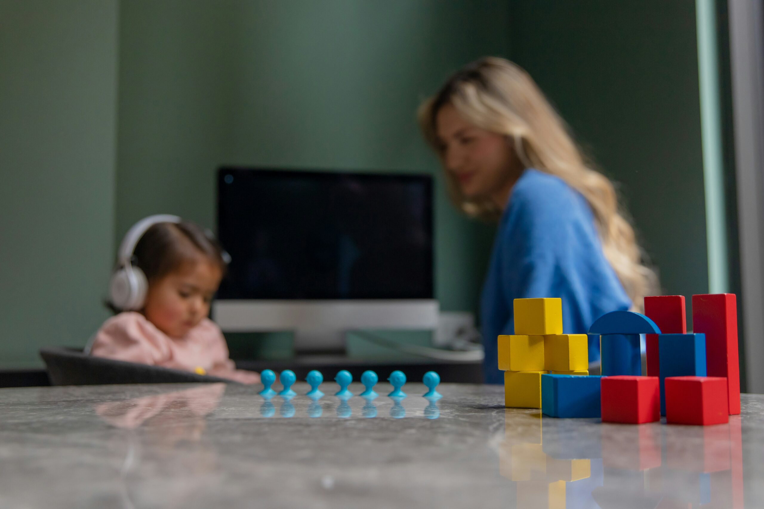 Two children play with colorful plastic building blocks on a table in a bright room, building a tower and structures in progress.